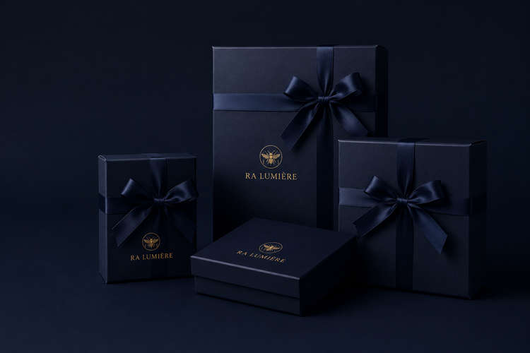 Ra Lumière Ritual Gifts wrapped in deep navy gift boxes with ribbons, featuring gold branding on a dark blue background.
